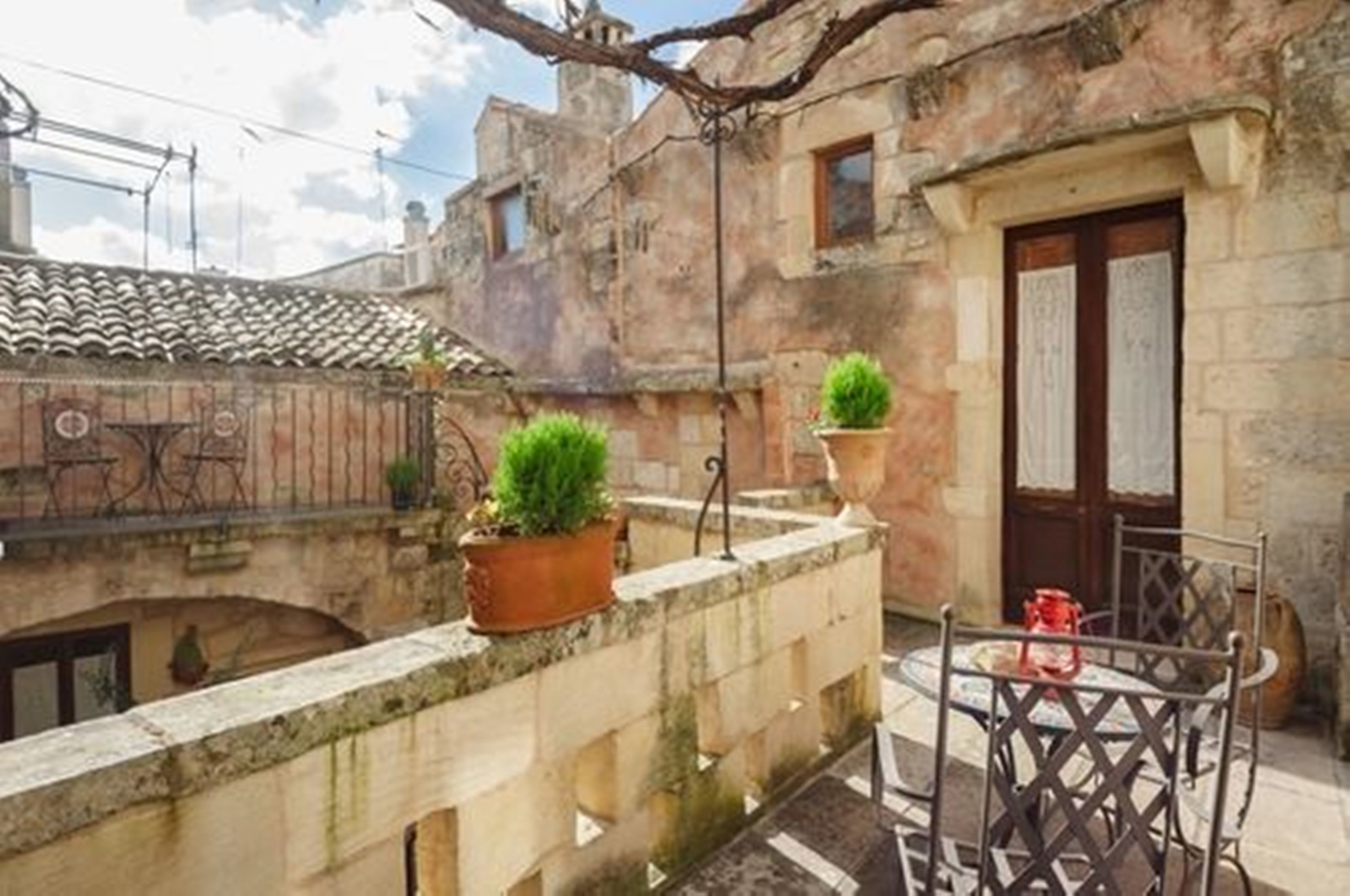 A courtyard with a stone wall, a small table with a chair, and potted plants.