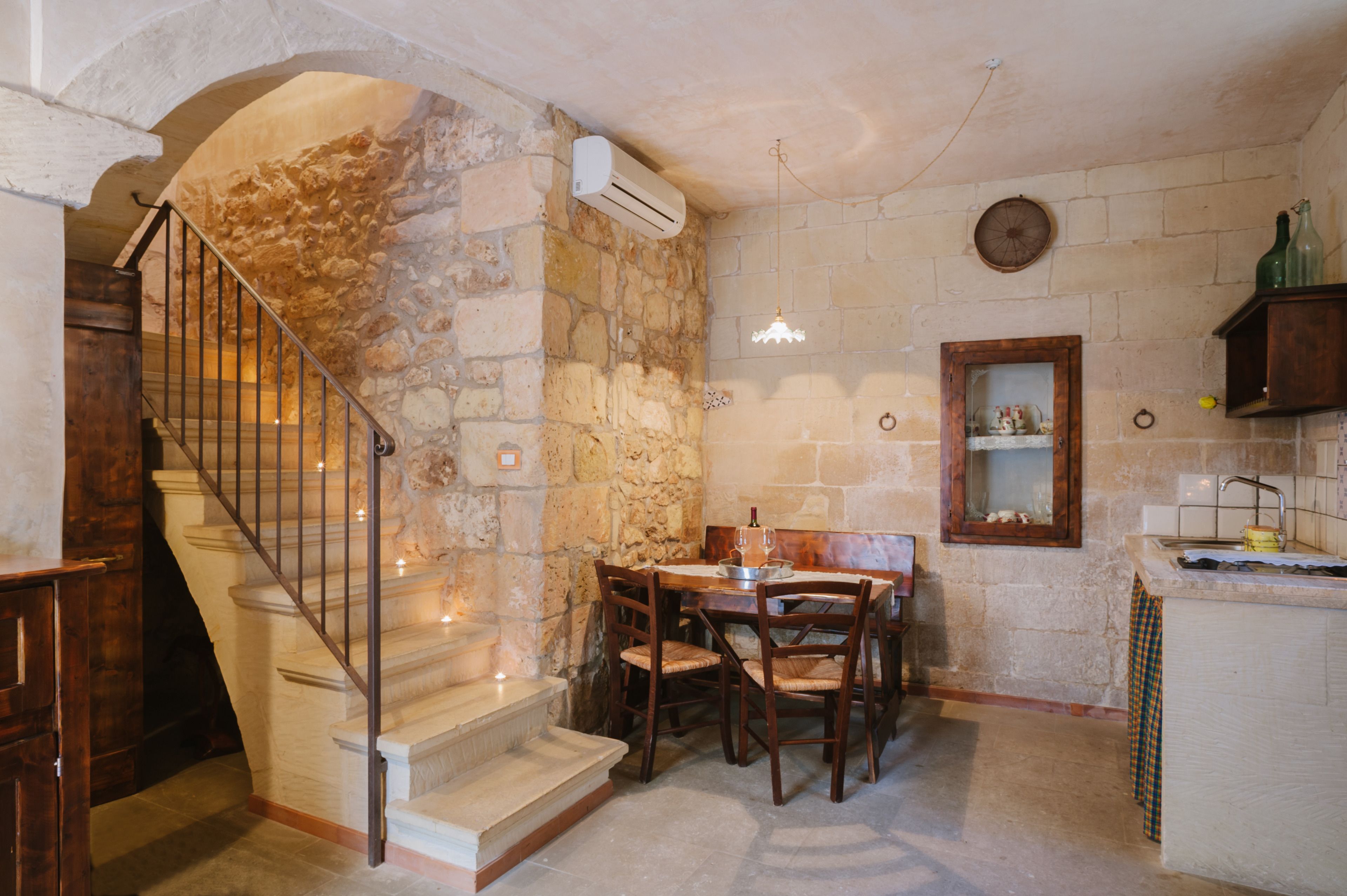 A stone-walled kitchen with a dining table, chairs, and a built-in sink.