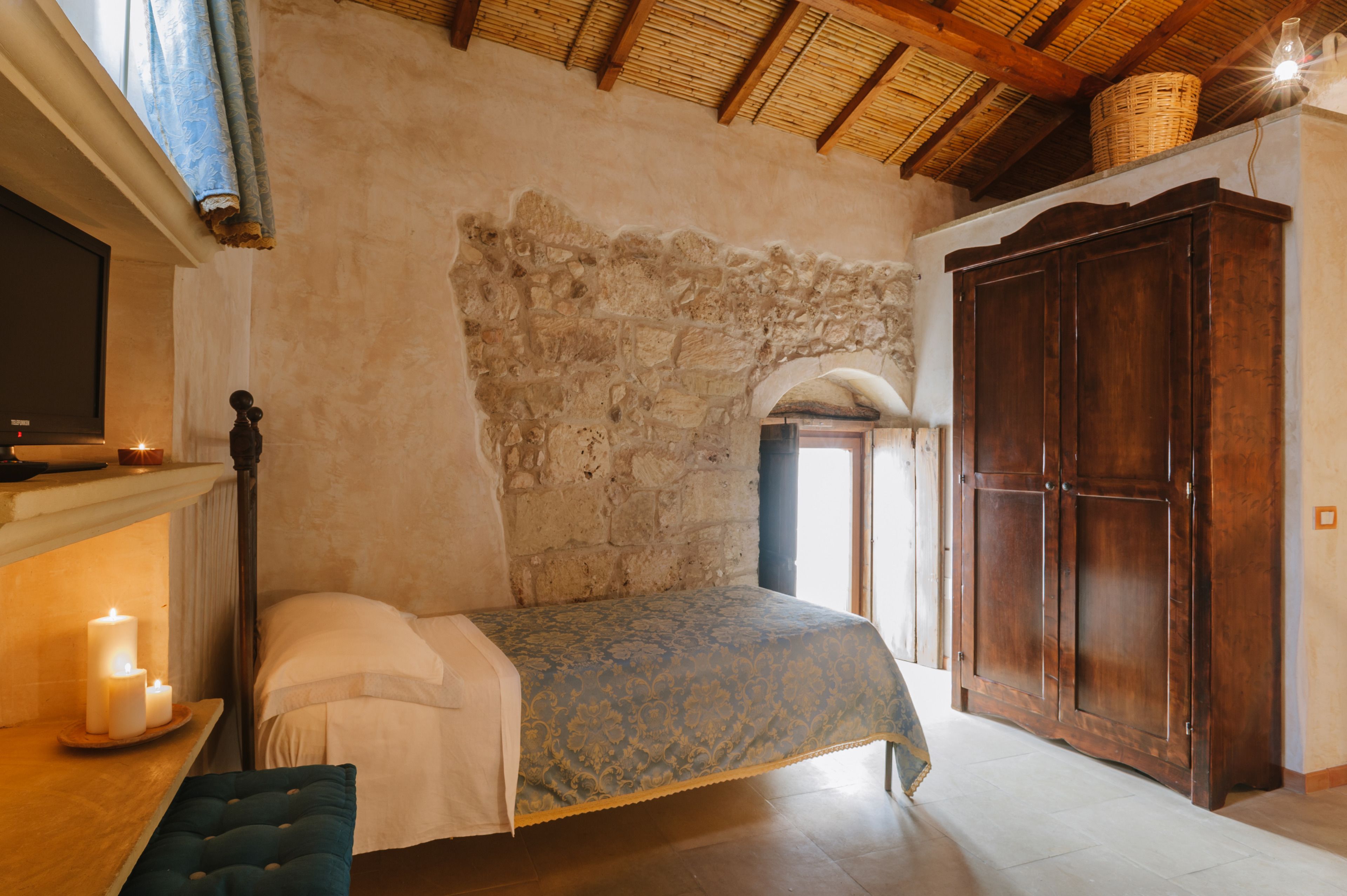 A bedroom with a stone wall, wooden wardrobe, and a bed with a blue bedspread.