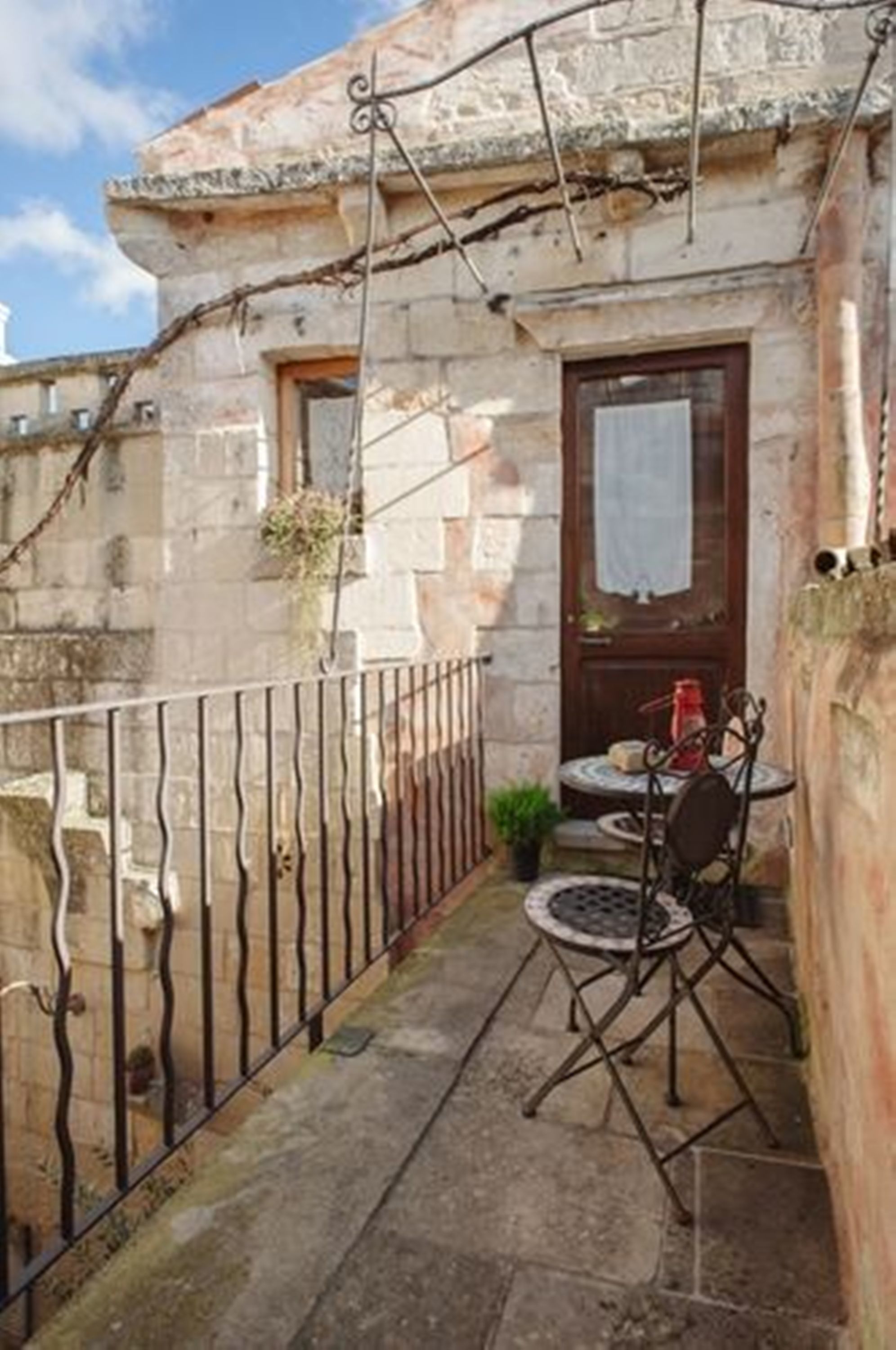 A stone building with a small balcony, a wooden door, and a metal chair.