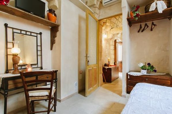 A bedroom with a wooden desk, chair, and dresser. There is a mirror on the wall, a bed with a white bedspread, and a door leading to another room.