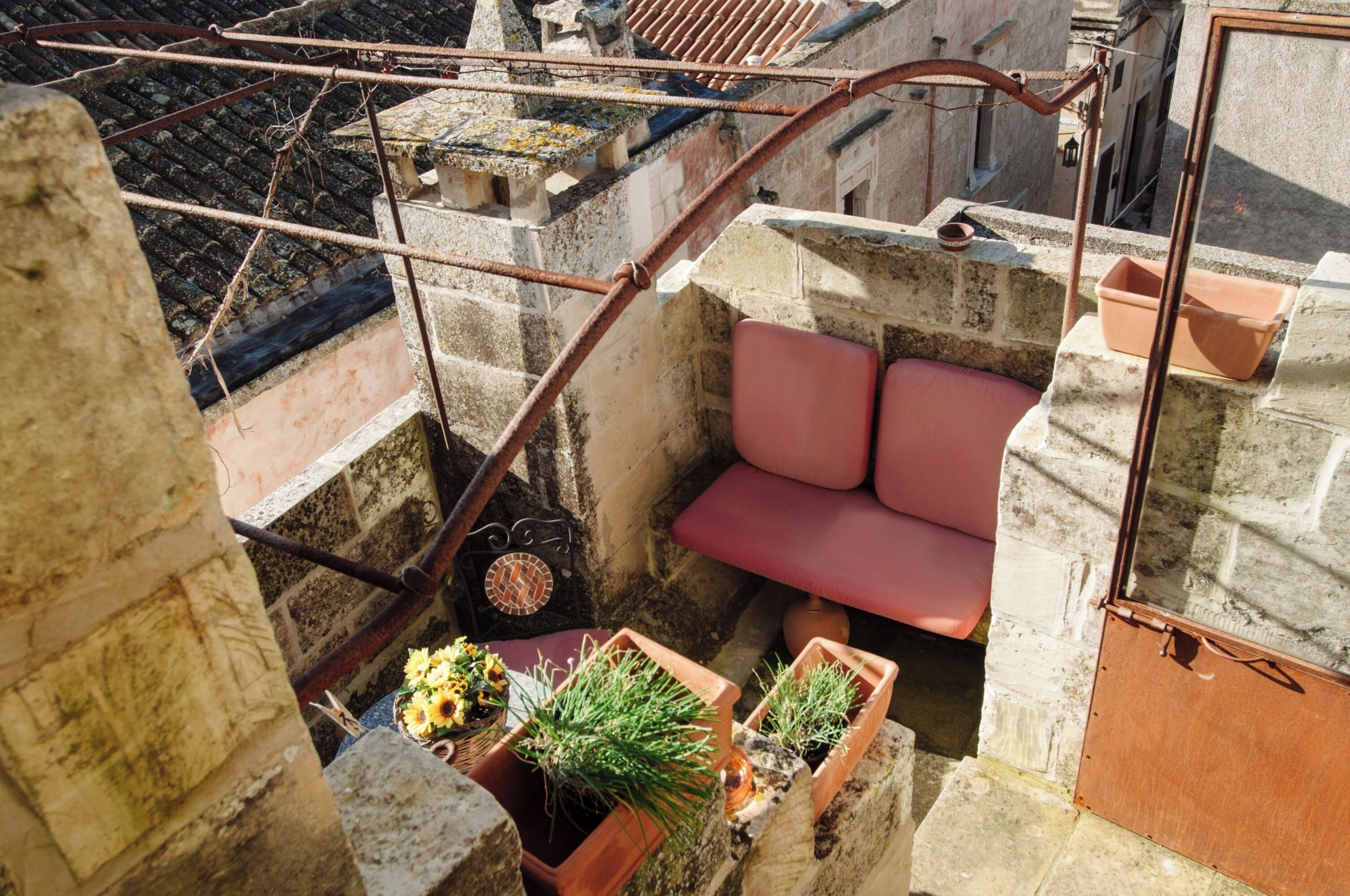 Ein kleiner Balkon mit einer roten Bank, Terrakottatöpfen mit Pflanzen und einem Metallgeländer.