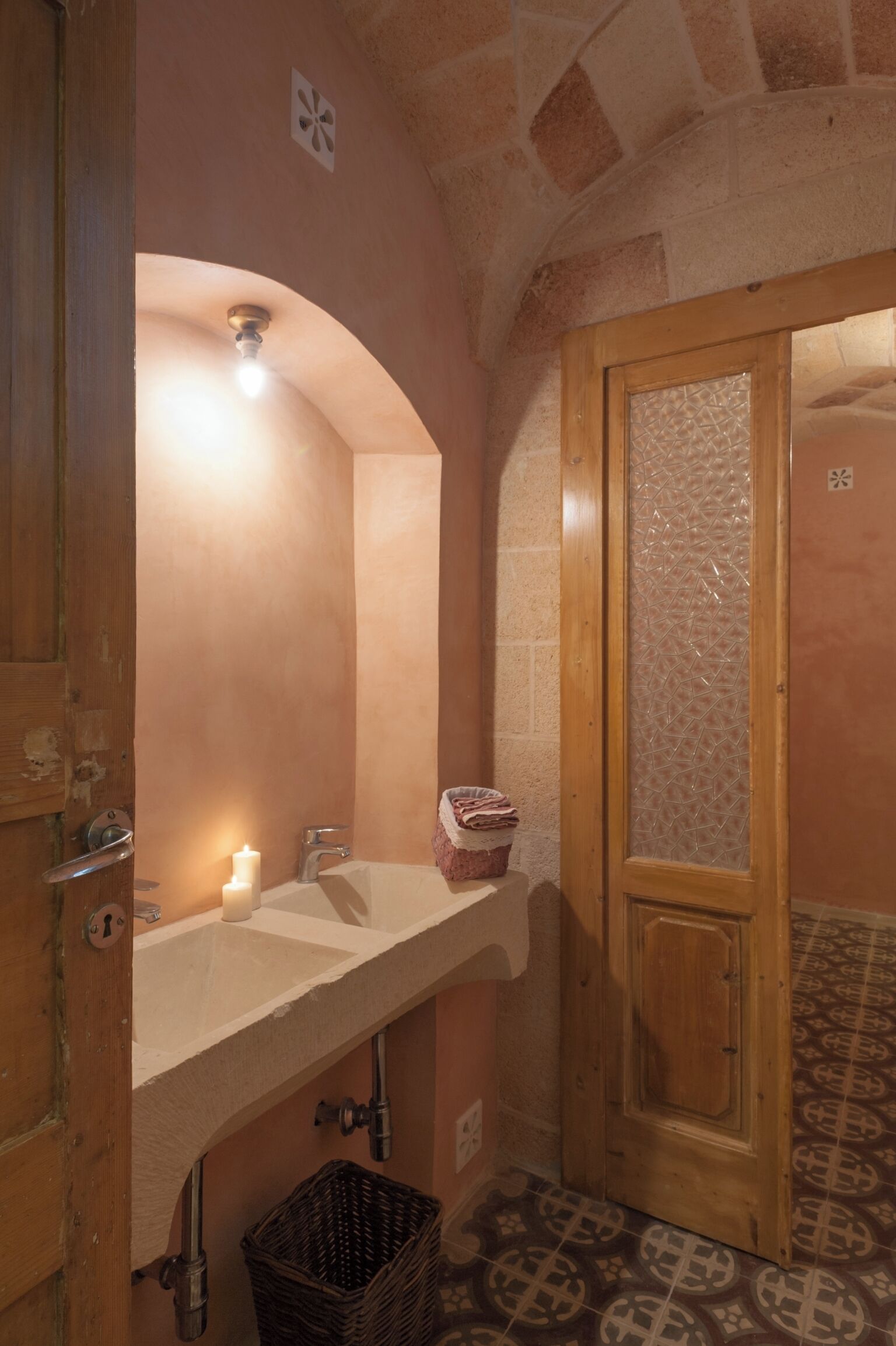 A bathroom with a white sink, a mirror, a wooden door, and a patterned floor.