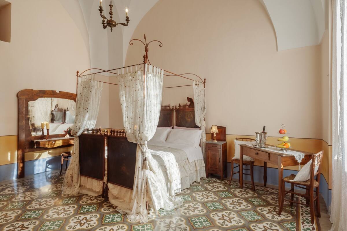Ein Schlafzimmer mit einem Himmelbett, einem Holztisch, einem Stuhl und einem Spiegel.