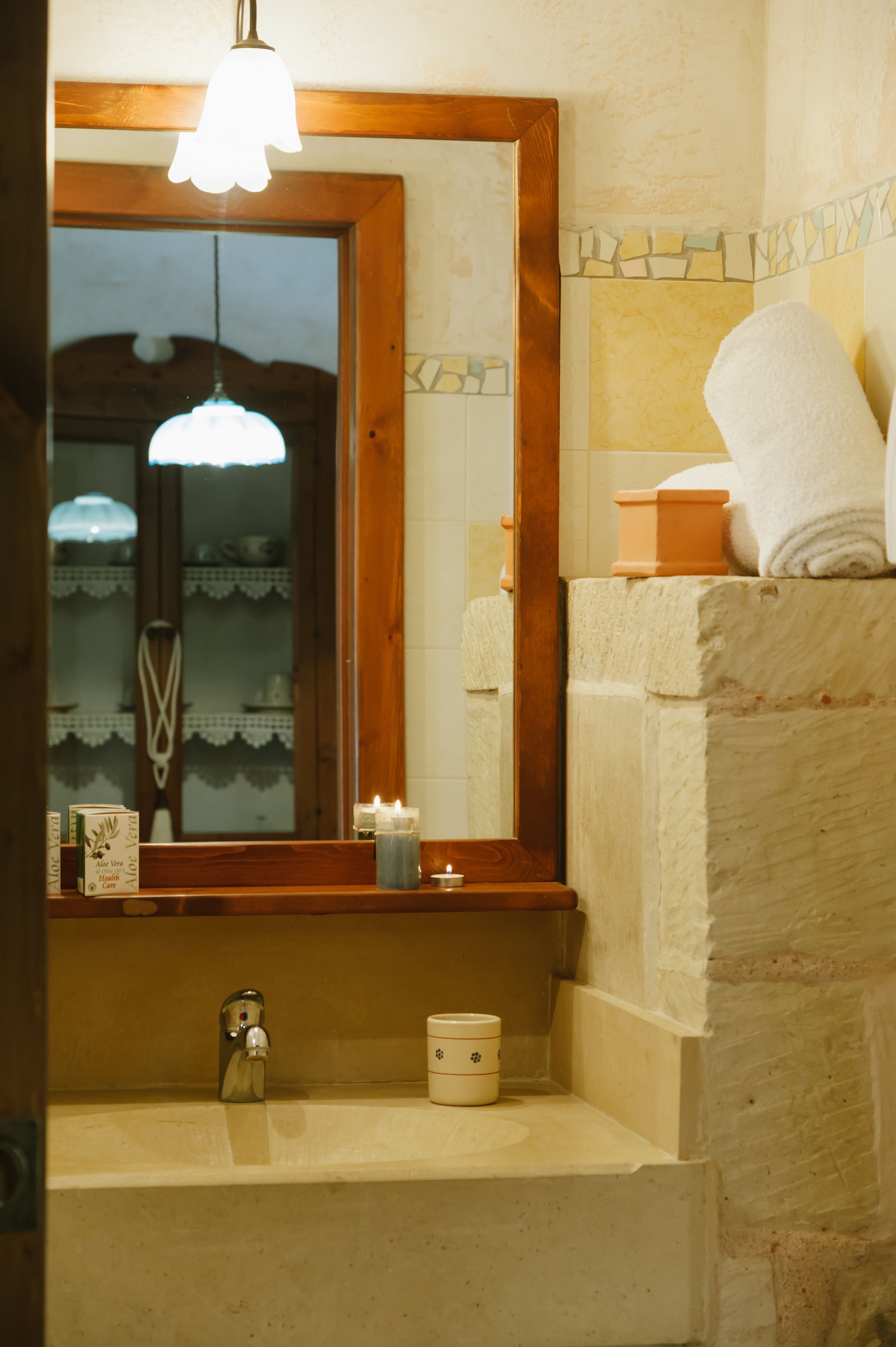 A bathroom with a wooden-framed mirror, a sink with a faucet, a candle, and a towel on a stone wall.
