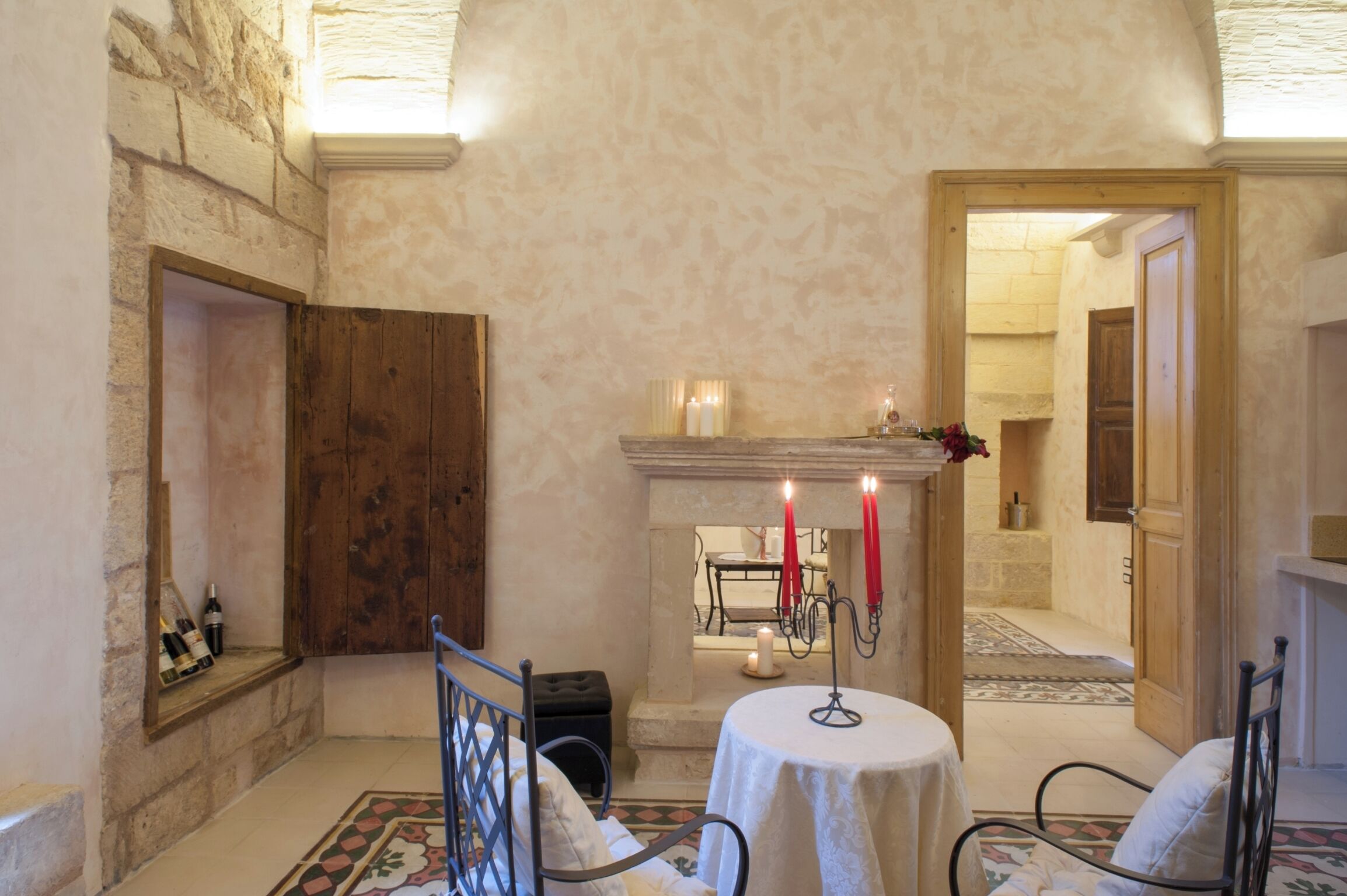 A room with a stone wall, a fireplace with candles, a round table, and a bench.