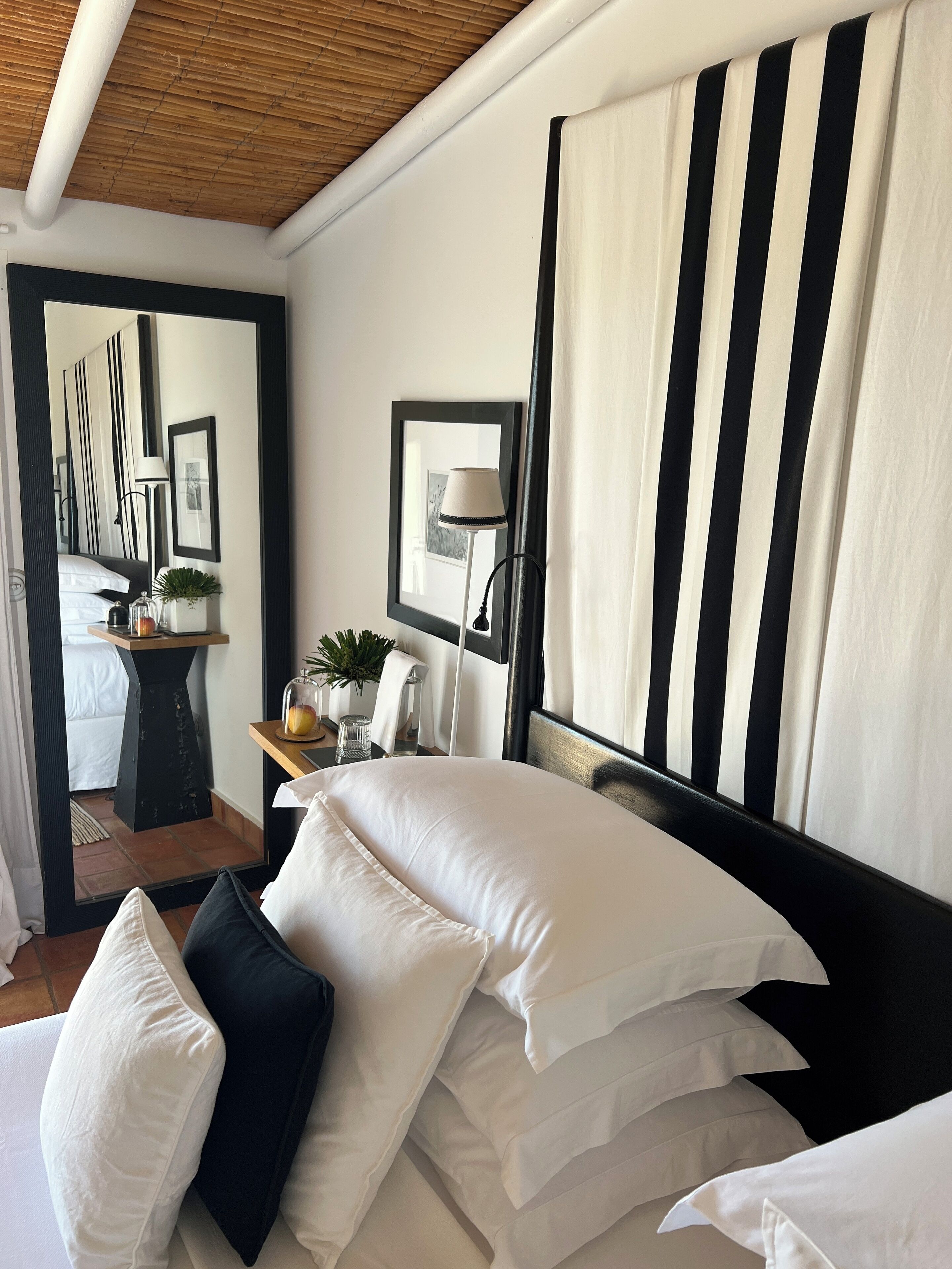 Habitación de hotel con cama, mesita de noche, lámpara y espejo.