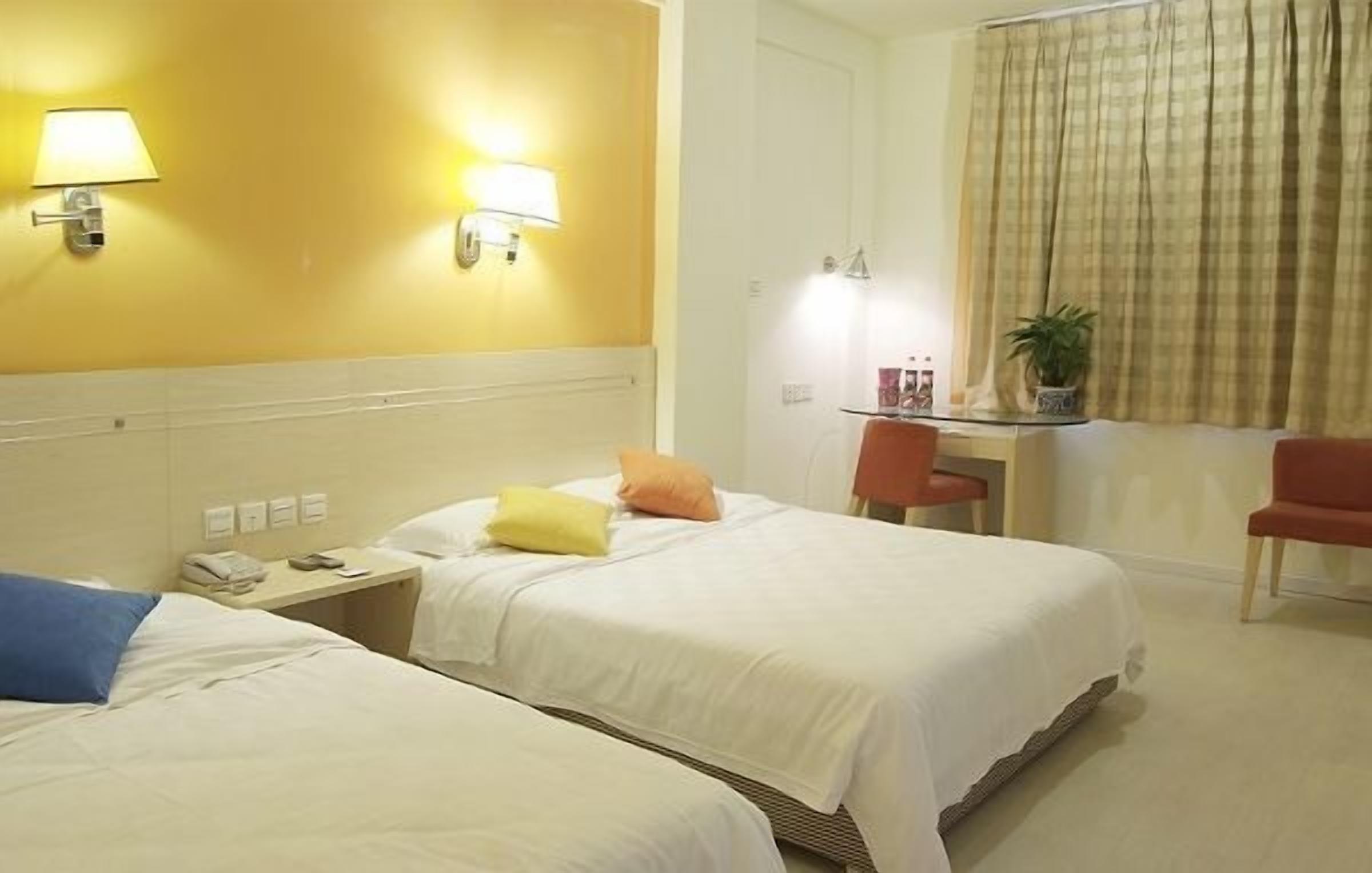 A hotel room with two beds, a desk, a chair, and a window with curtains.