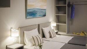 Una camera d'albergo con due letti, un quadro, un armadio e un comodino con una lampada.