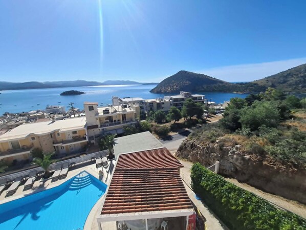 A coastal hotel with a swimming pool, terracotta roof, and views of the sea and hills.