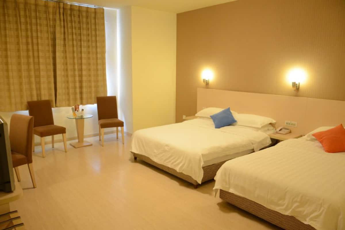Quarto de hotel com duas camas, uma mesa pequena e cadeiras, e uma televisão.