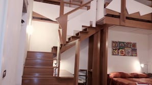 A wooden staircase leading to a bedroom with a bed and a quilted wall hanging. - Amedeo (Naples)