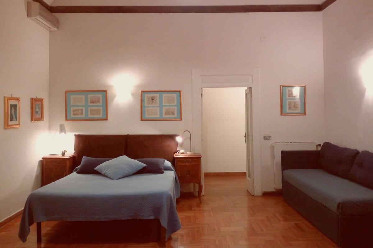 A bedroom with a bed, a nightstand, a dresser, a radiator, and a door leading to another room.