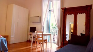 A room with a wooden floor, a blue sofa, a dining table with chairs, a TV, and a wardrobe. - Amedeo (Naples)