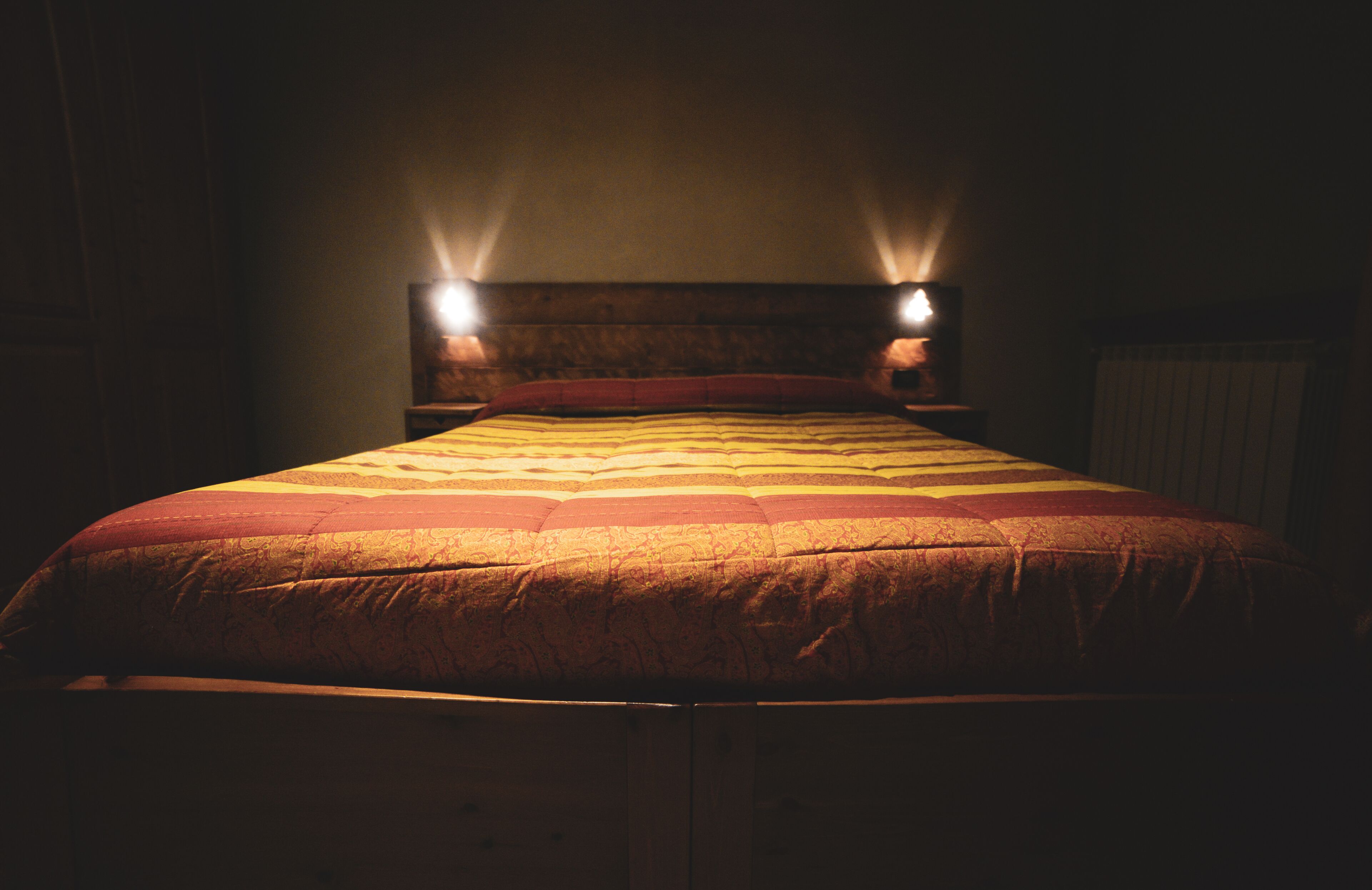 A bed with a wooden headboard and two wall-mounted lights.