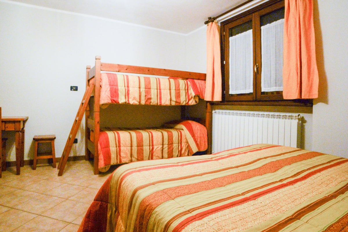 A dormitory room with bunk beds, a small table, and a window with curtains.