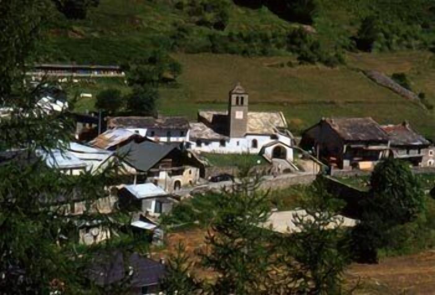 A small village with traditional buildings, including a church with a bell tower, surrounded by greenery.