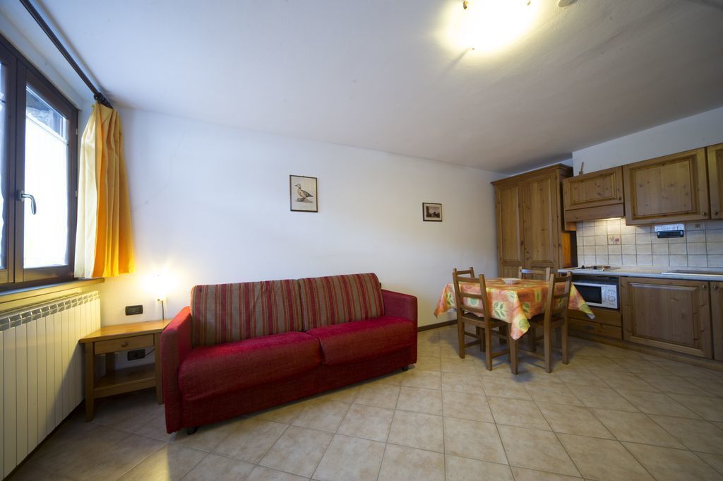 Ein kompakter Wohnraum mit einem roten Sofa, einem Esstisch mit Stühlen, Holzschränken und einem Fenster mit Vorhängen.