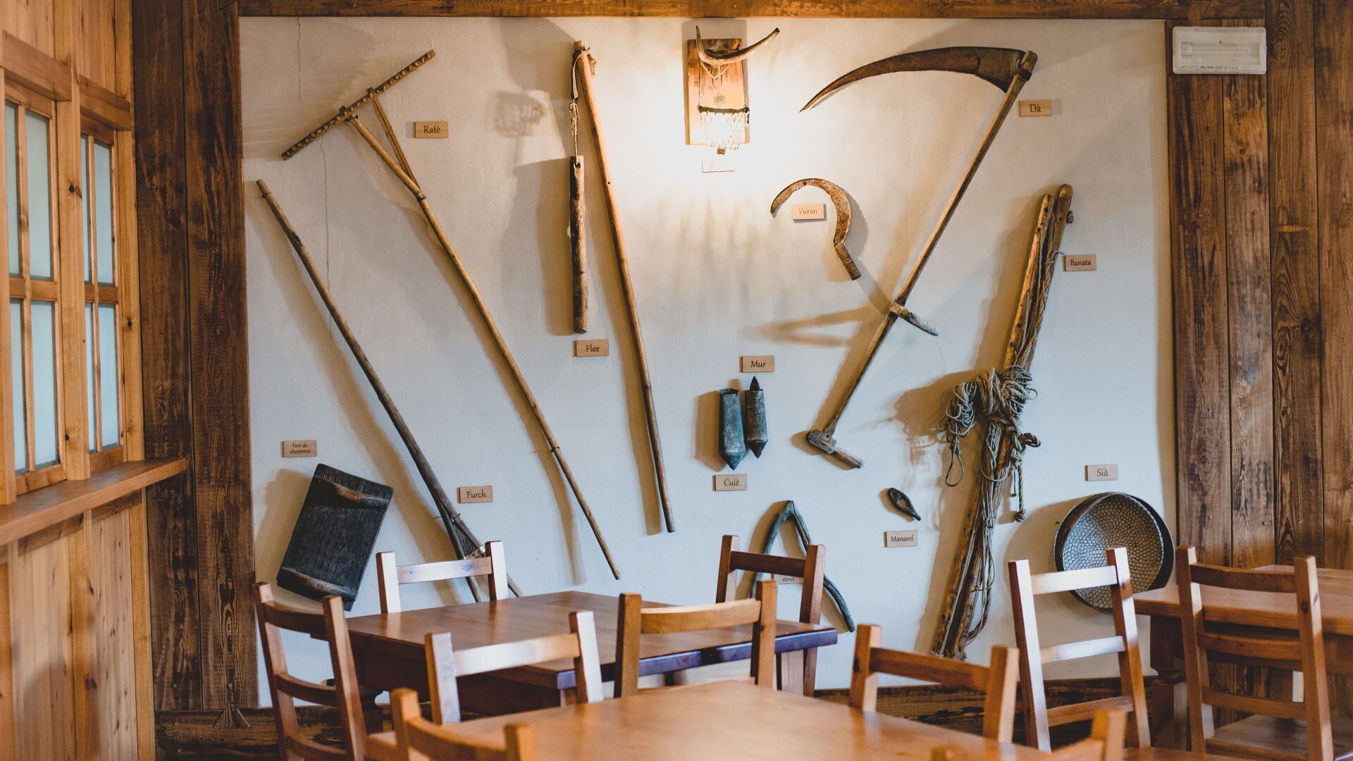Un intérieur rustique en bois, agrémenté d’une collection d’outils agricoles exposés au mur.