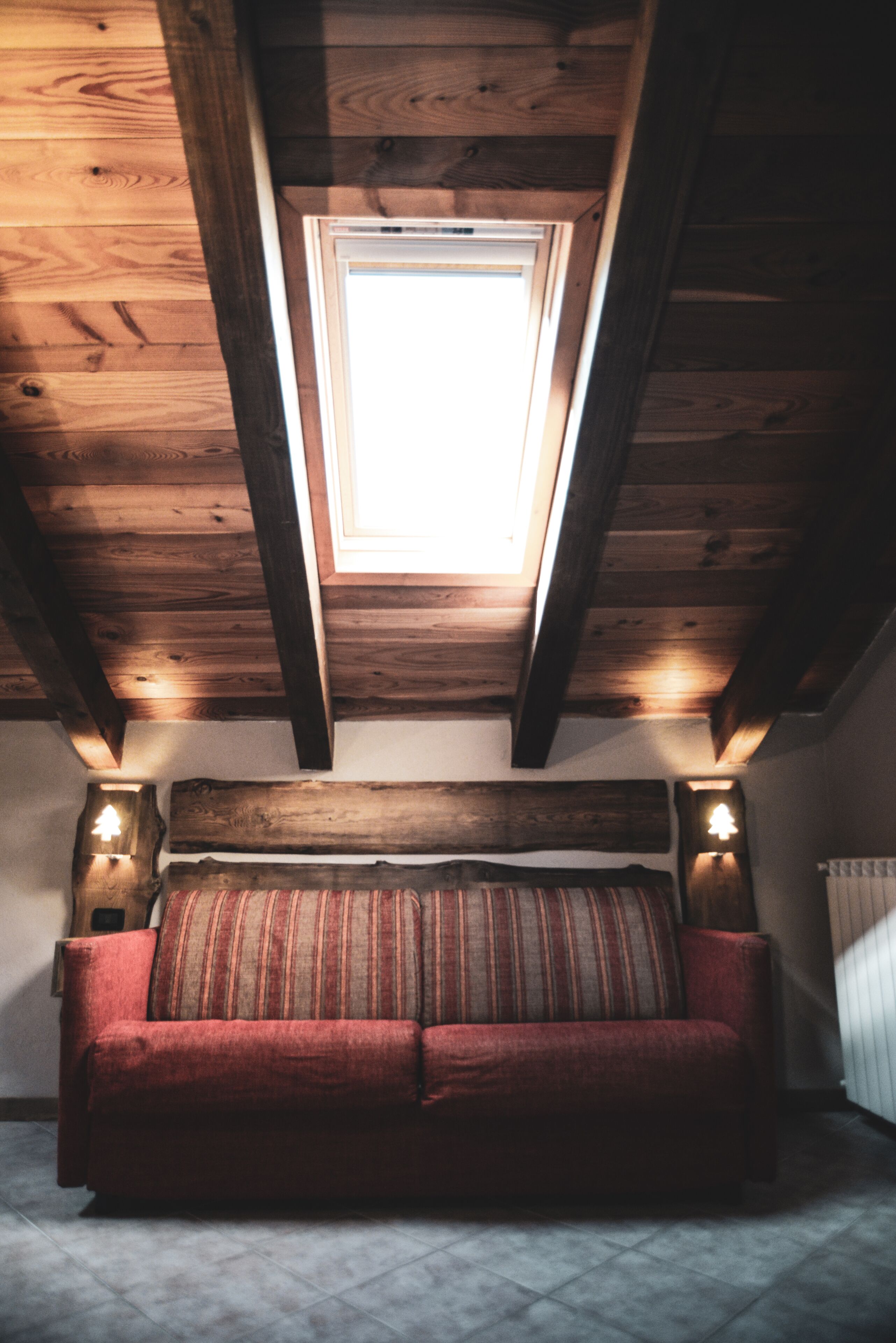 Ein gemütliches Zimmer mit Holzboden, einem schrägen Oberlicht, einem roten Sofa und zwei Wandleuchten.