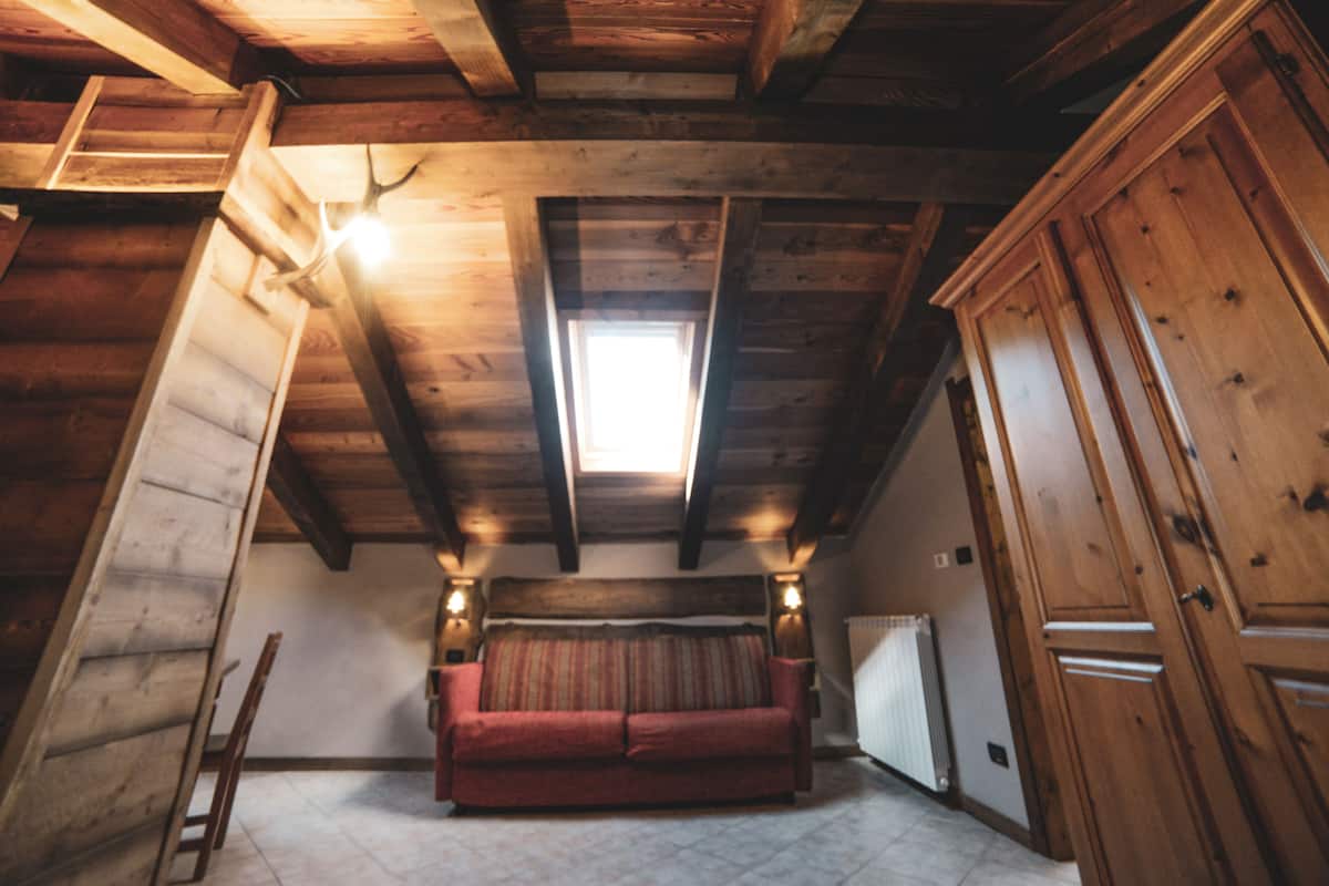 A wooden cabin interior with a loft bed, a red sofa, and a wooden wardrobe.