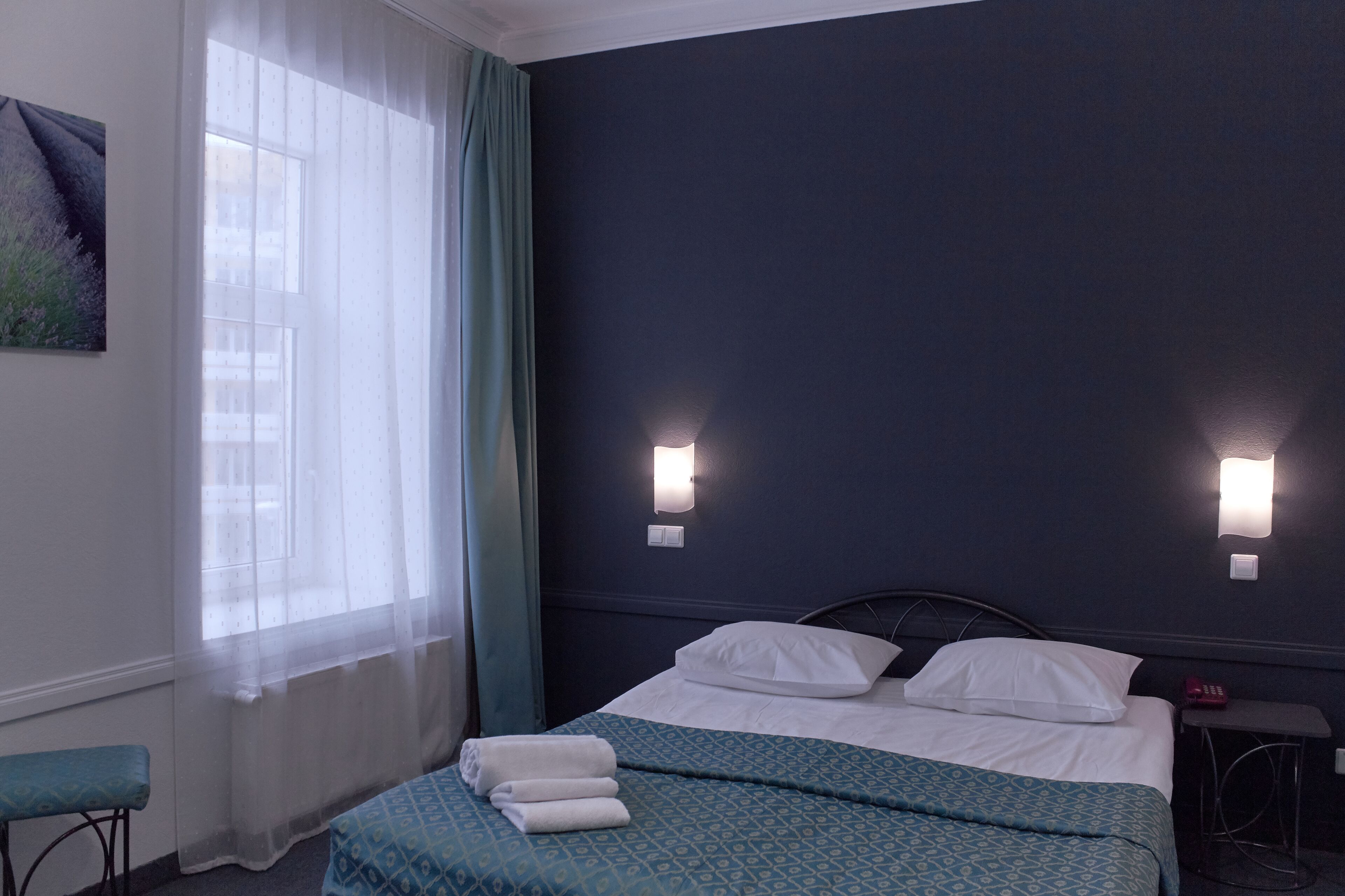 Ein Hotelzimmer mit Bett, einer Bank, einem Fenster mit Vorhängen und Wandleuchten.