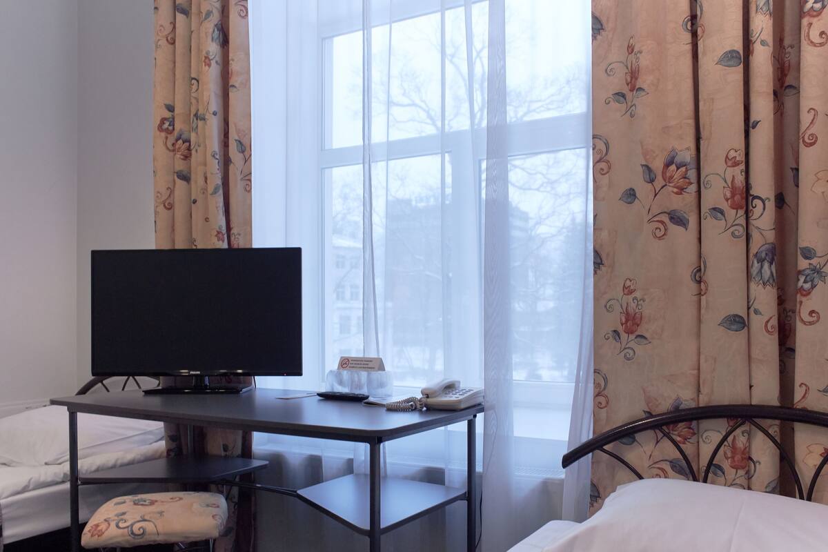 A hotel room with a bed, a desk with a television, a telephone, and a window with curtains.