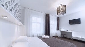 A modern hotel room with a large bed, a desk, a chair, a flat-screen TV, and a chandelier. - Hotel OK (Riga)