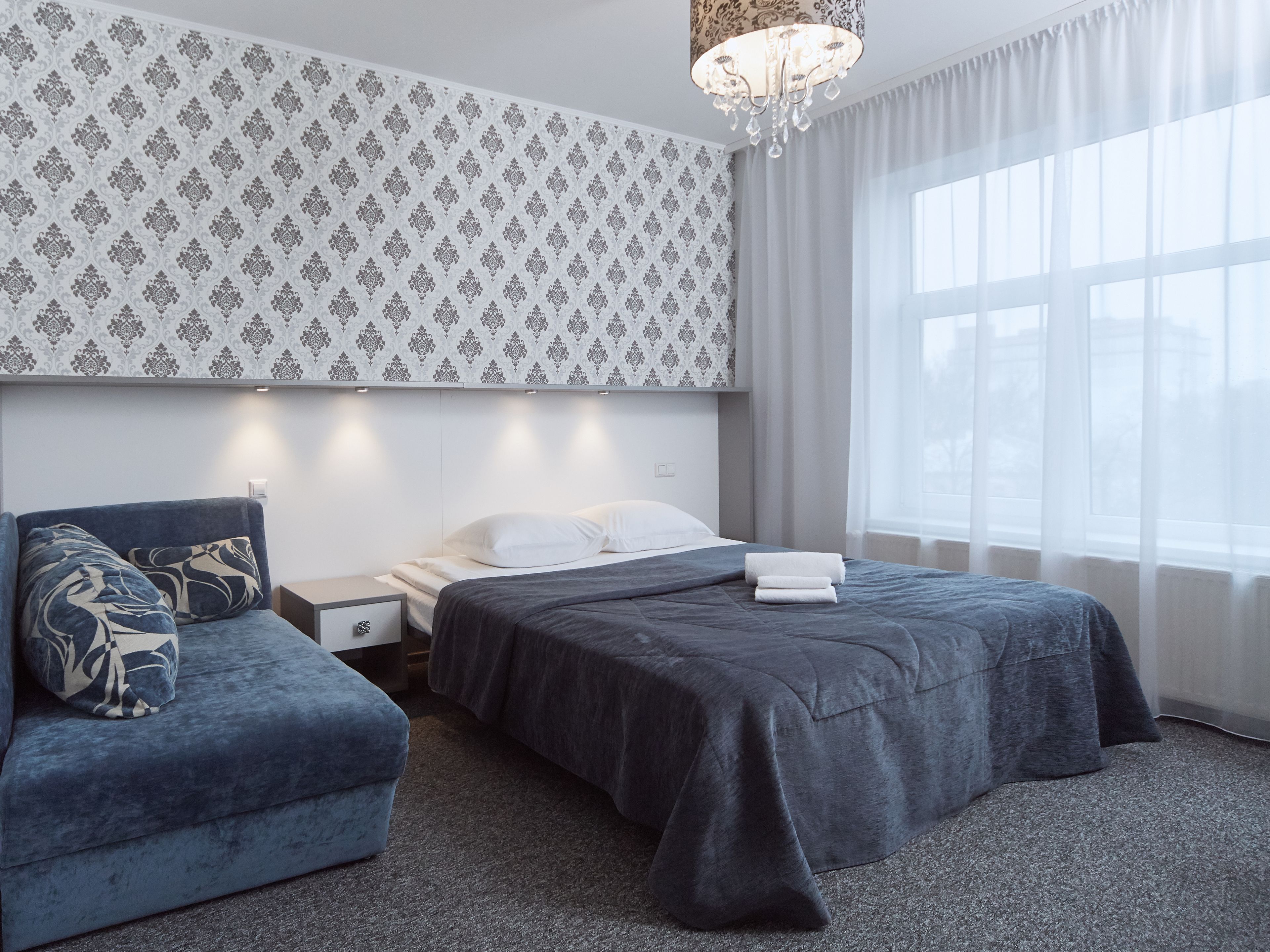 Moderni hotellihuone, jossa on suuri sänky, sohva, yöpöytä ja kattokruunu.
