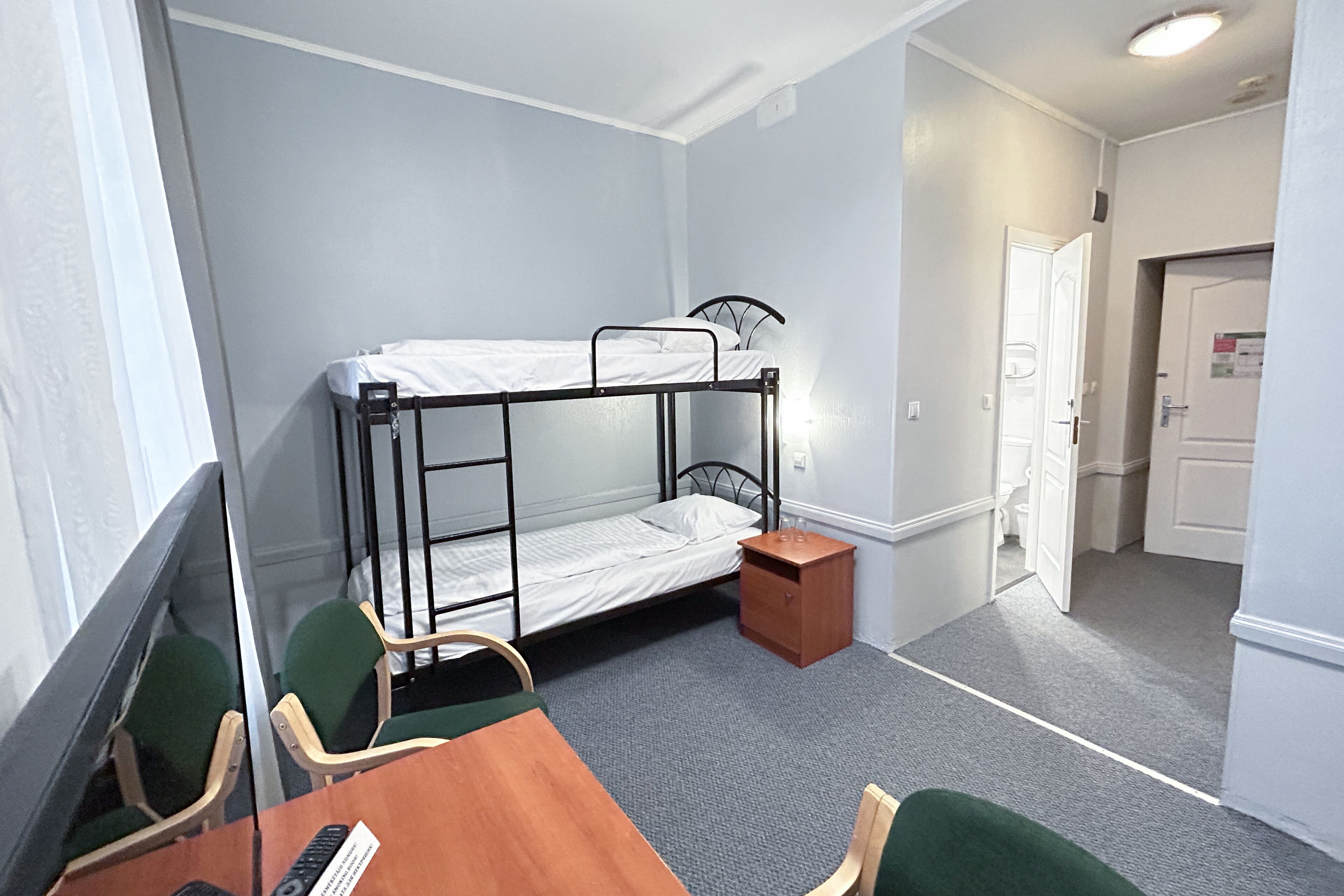 A dormitory room with bunk beds, a small wooden table, two chairs, and a desk.