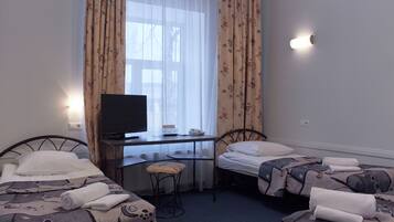 Habitación de hotel con dos camas, un escritorio con televisor y una ventana con cortinas florales.