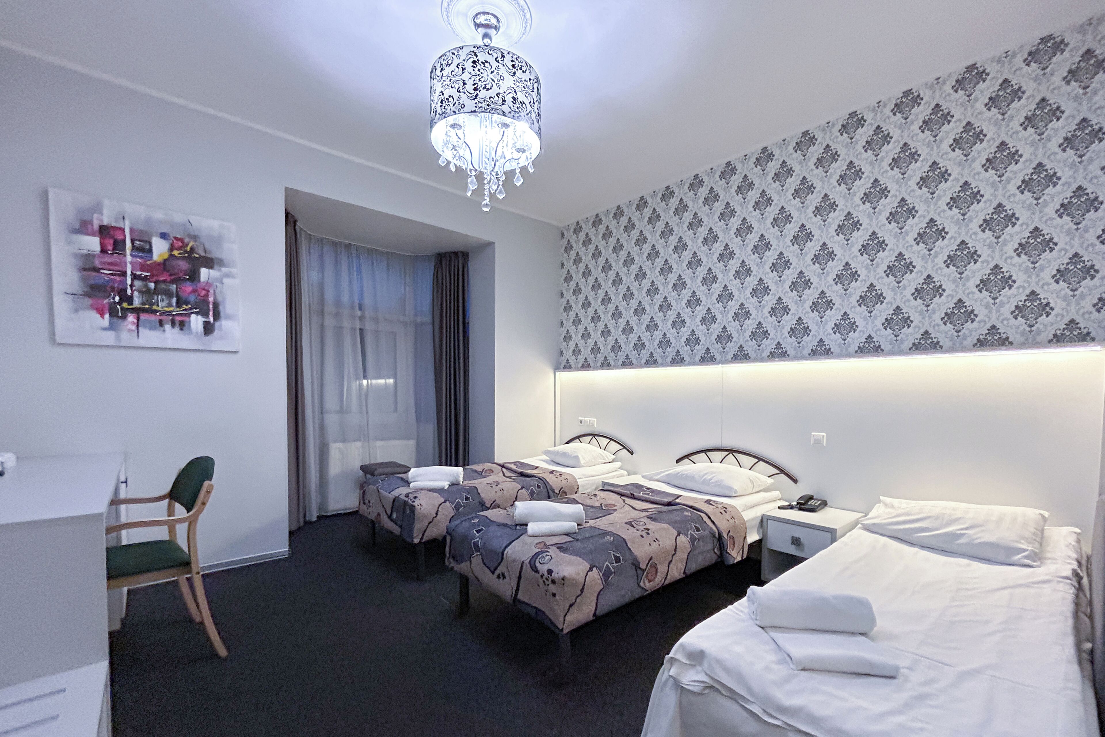 Habitación de hotel con dos camas, un escritorio, una silla, una araña y papel tapiz estampado.