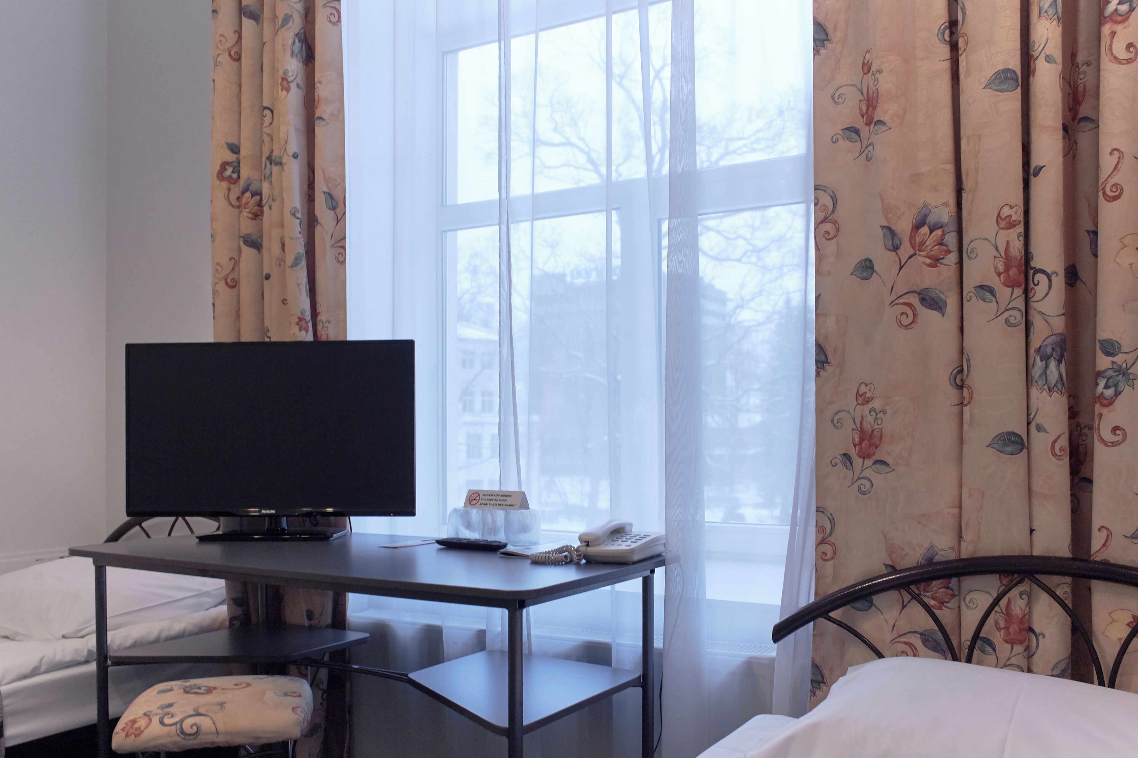 Habitación de hotel con cama, escritorio con televisor, teléfono y ventana con cortinas.
