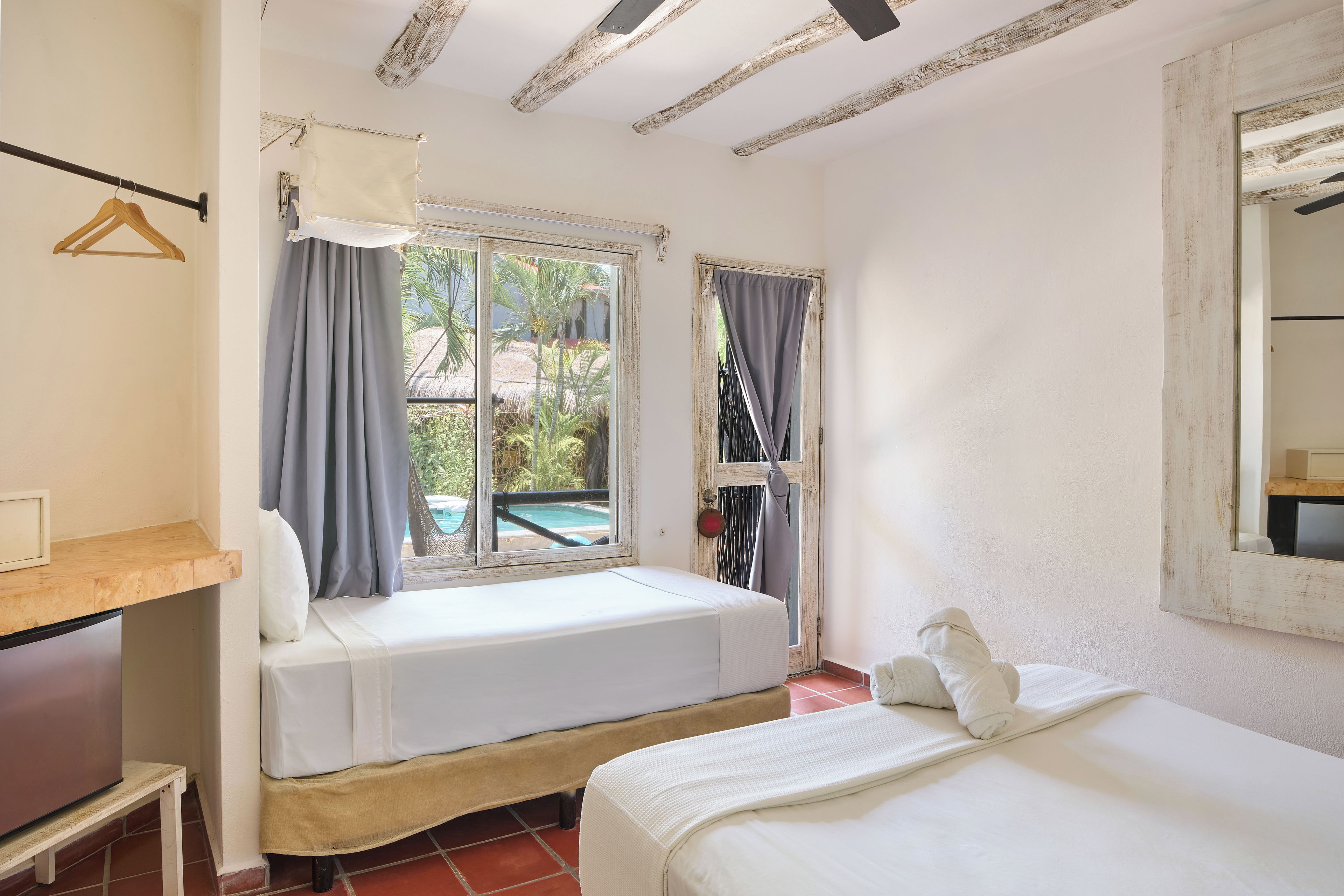 A room with two beds, a wooden table, a hanging clothes rack, and a window with curtains.