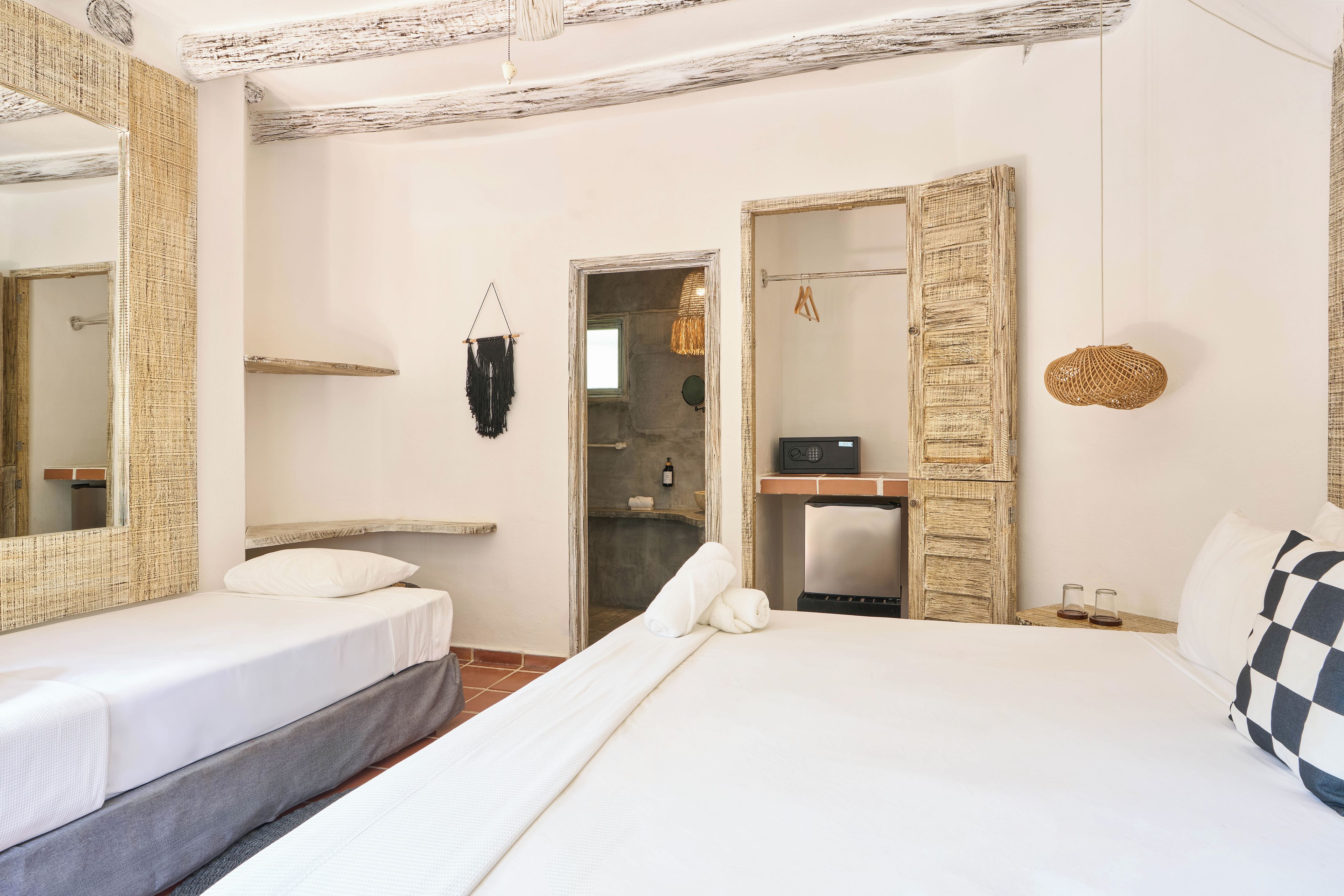 A hotel room with two beds, a large mirror, a wardrobe, and a bathroom visible through an open door.