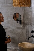 Un baño con un espejo redondo, un lavabo de madera y un grifo de pared.