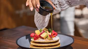 A stack of pancakes with fruit toppings and syrup being poured on top.
