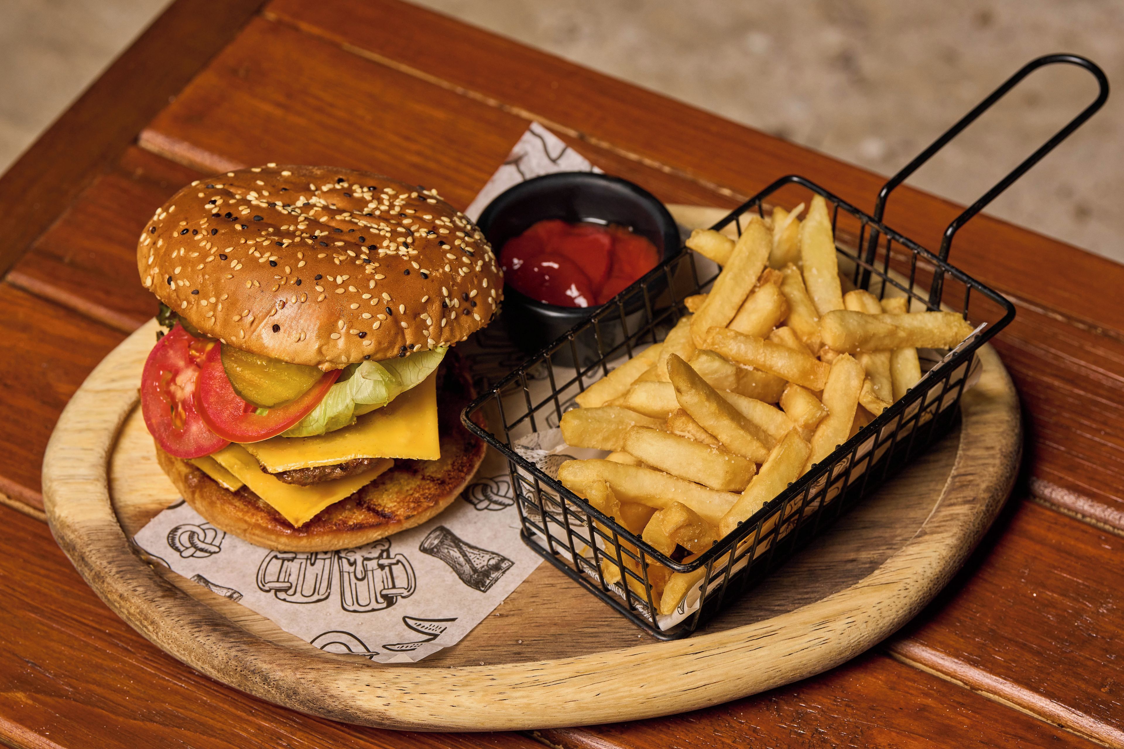 Una comida que incluye una hamburguesa con lechuga, tomate y queso, una porción de papas fritas y un recipiente pequeño de kétchup.