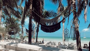 Un bar situé en bord de mer, avec des tables à l’extérieur, un hamac et des palmiers.