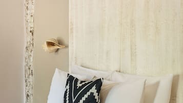 A bed with white bedding and a black and white patterned pillow, a textured wall, and a simple headboard.