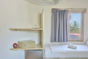 A compact room with a bed, a small table, a shelf with glasses, and a window with curtains. - Holbox Dream Beach Front Hotel  (Isla Holbox)