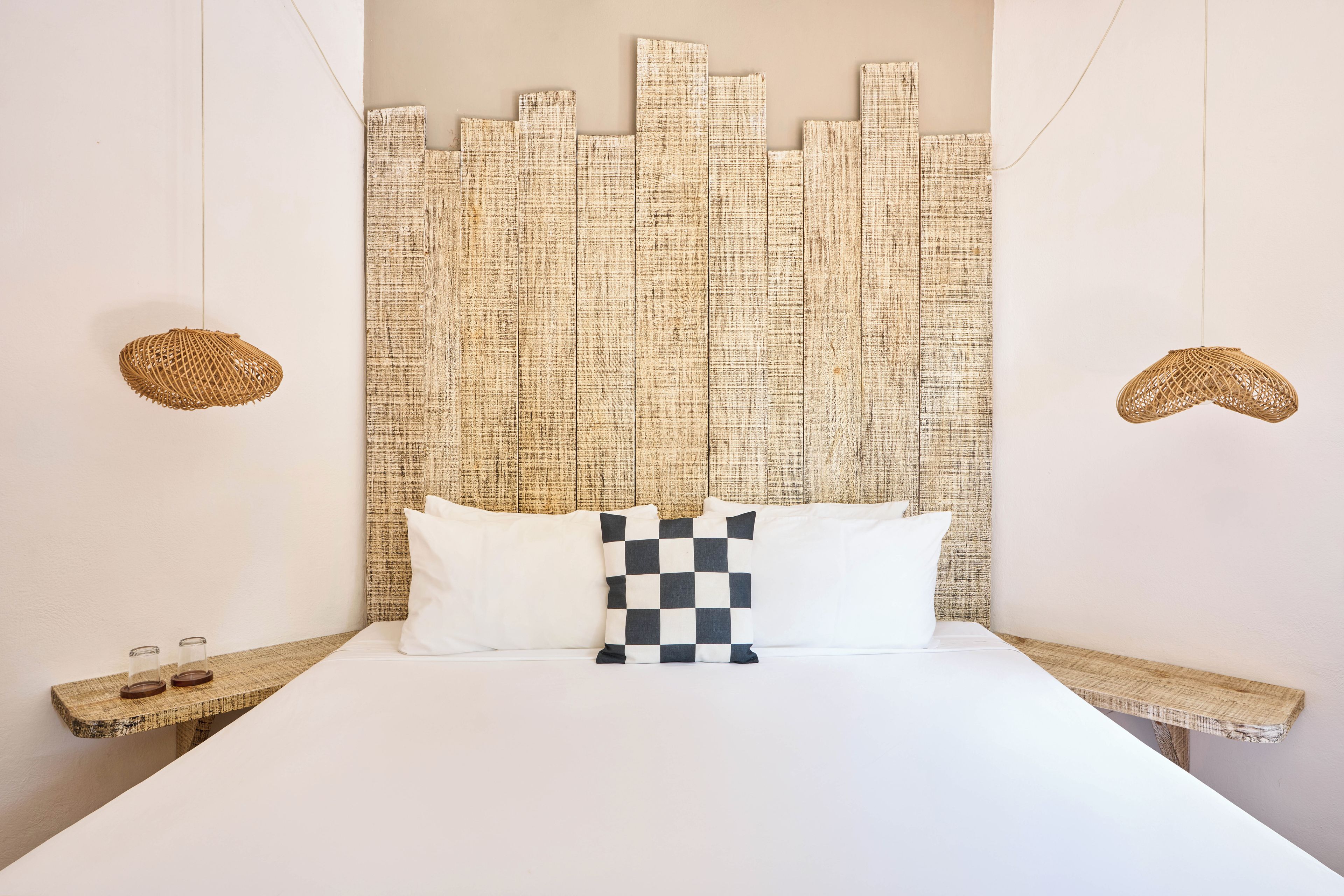 Una cama con un cojín de cuadros, dos mesitas de noche tejidas y un panel de pared con textura.