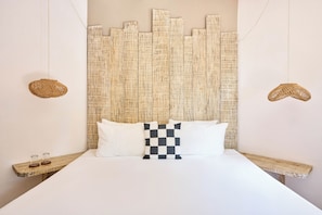 A bed with a checkered pillow, two woven nightstands, and a textured wall panel. - Holbox Dream Beach Front Hotel  (Isla Holbox)