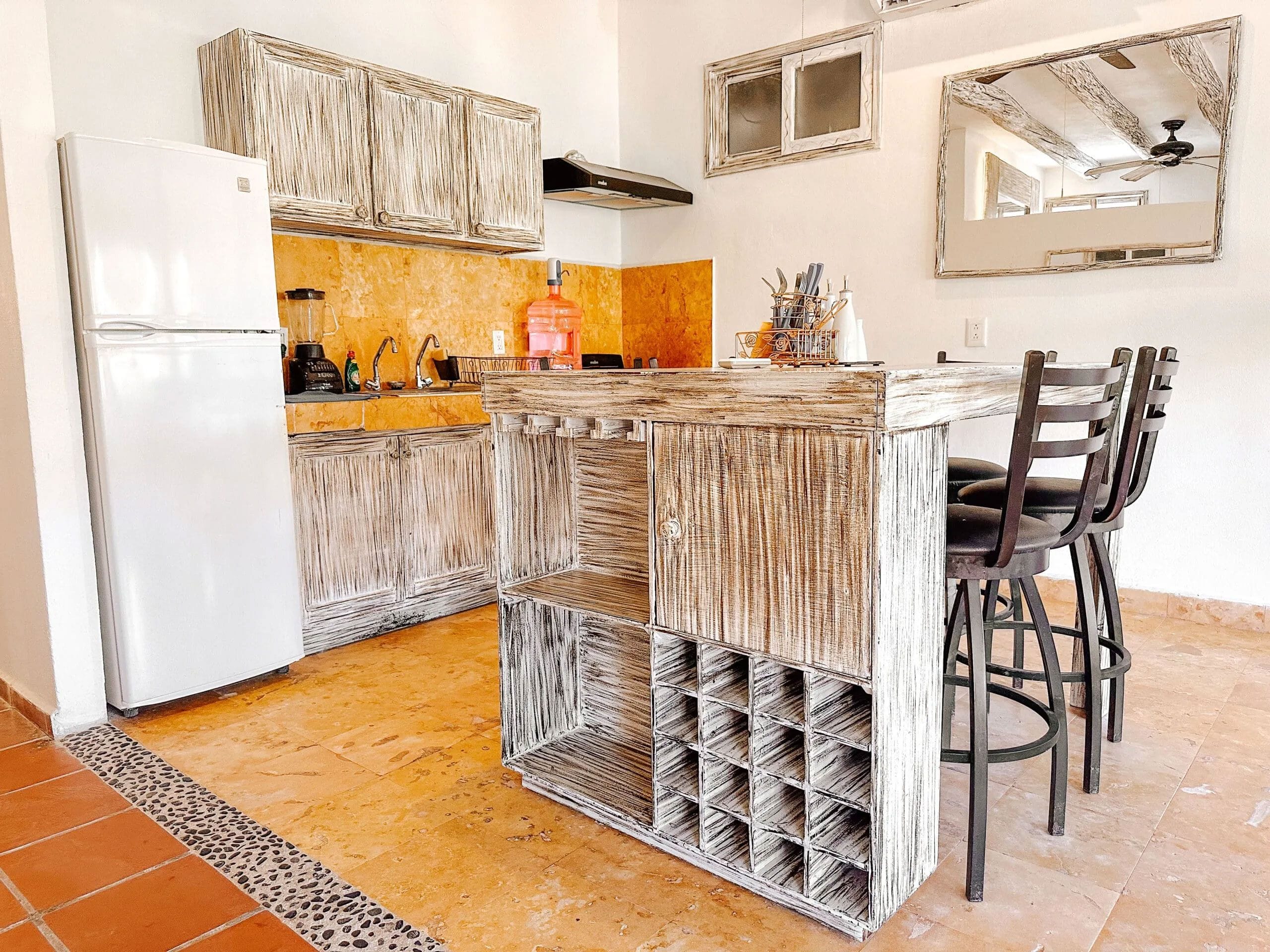 Una cocina con refrigerador blanco, armarios de madera, una barra con taburetes y piso de baldosas.