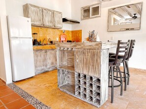 A kitchen with a white refrigerator, wooden cabinets, a bar counter with stools, and a tiled floor. - Holbox Dream Beach Front Hotel  (Isla Holbox)