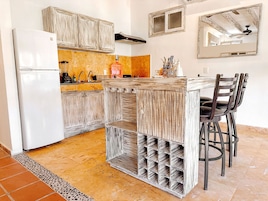 Una cocina con refrigerador blanco, armarios de madera, una barra con taburetes y piso de baldosas.