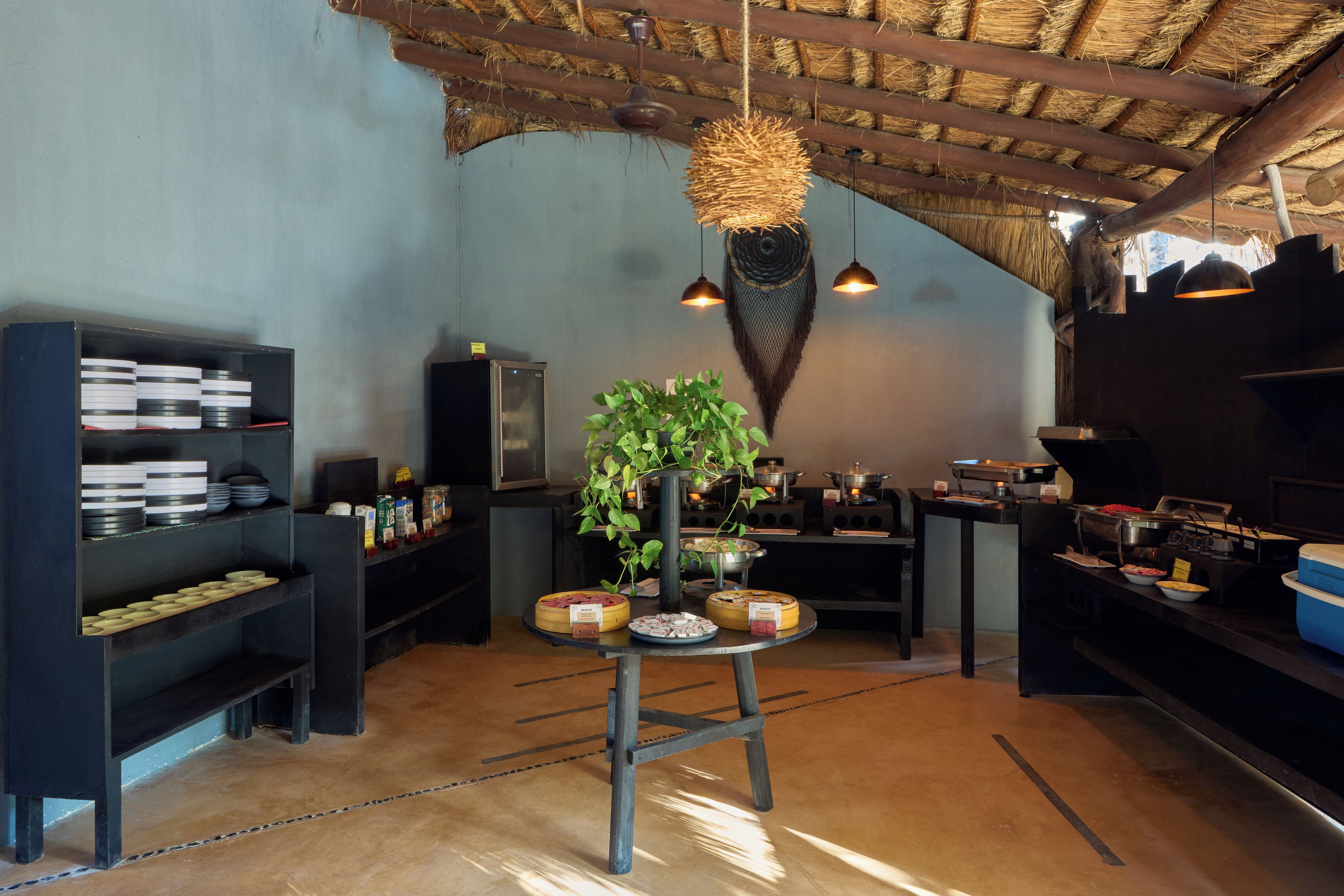 A restaurant interior with a rustic ceiling, shelves with plates, a central table with a plant, and a buffet area.