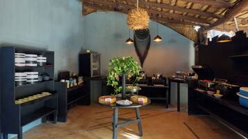 A restaurant interior with a rustic ceiling, shelves with plates, a central table with a plant, and a buffet area.