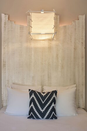 Un lit avec deux oreillers, l’un uni et l’autre à motifs en zigzag, adossé à un mur texturé avec un luminaire au-dessus.