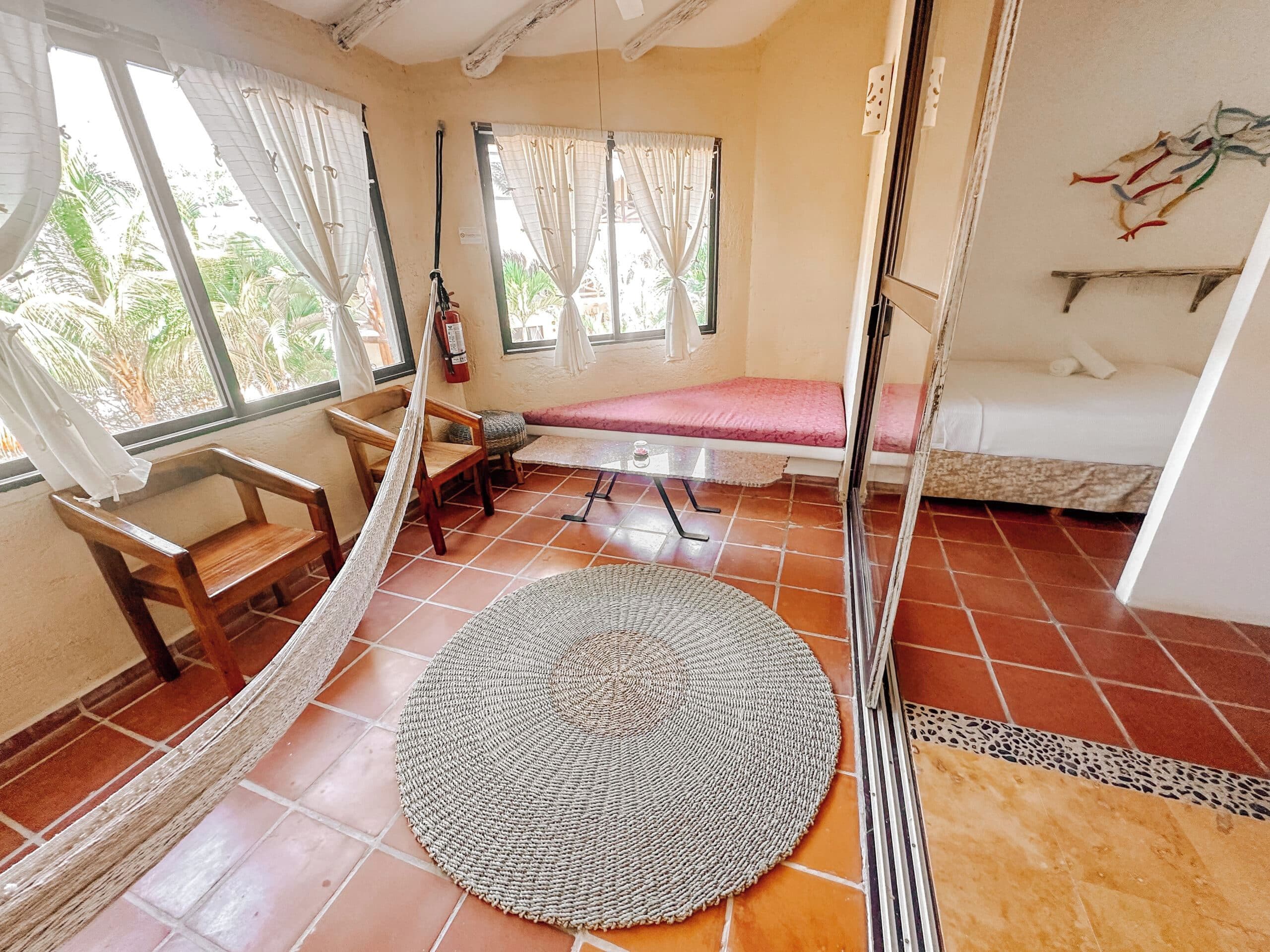 A room with a hammock, a round woven mat, a bed, and a bench.